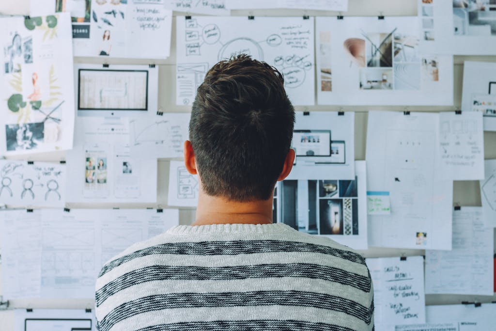 Man Wearing Black and White Stripe Shirt Looking at White Printer Papers on the Wall