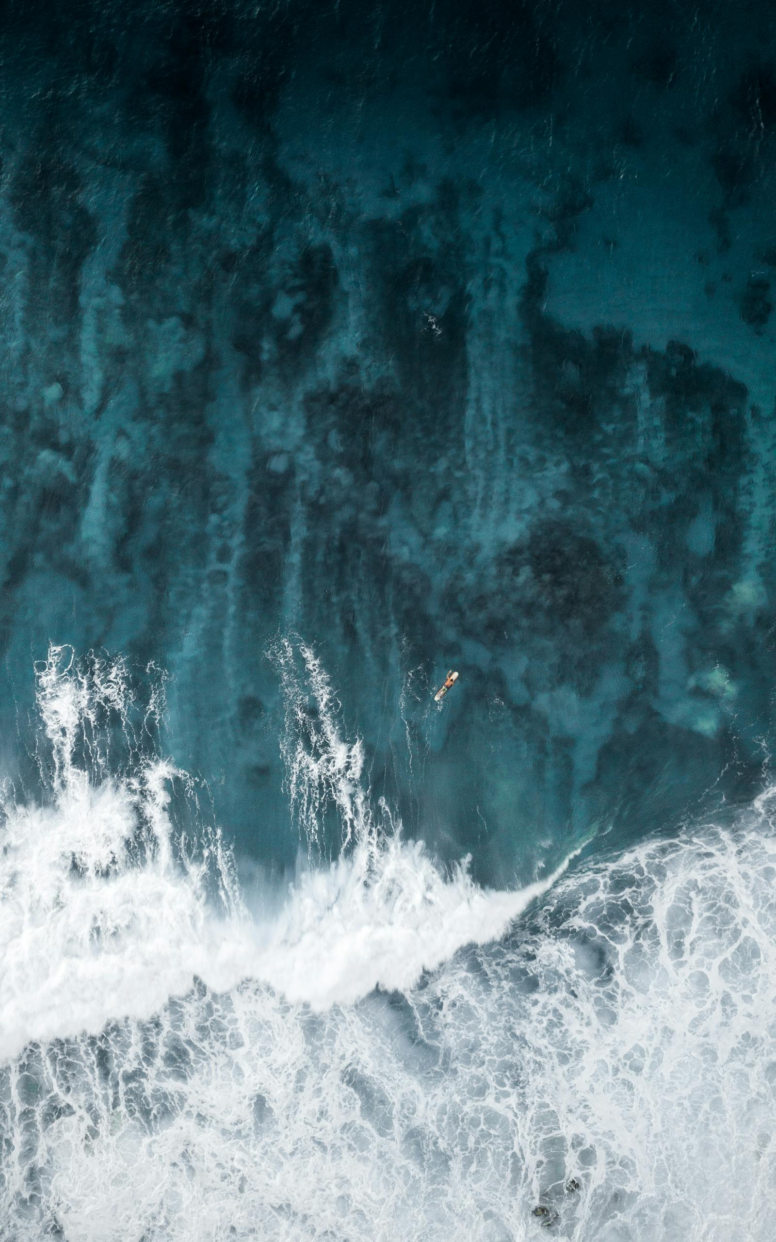 A breathtaking aerial view of a lone surfer navigating the ocean waves.